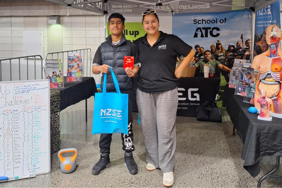Young boy who has won competition standing next to staff with his award NZSE